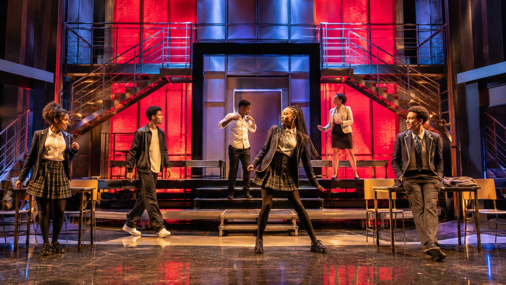 A bright contemporary live-theatre set with scaffolding, stairs, platforms and strong saturated colour.